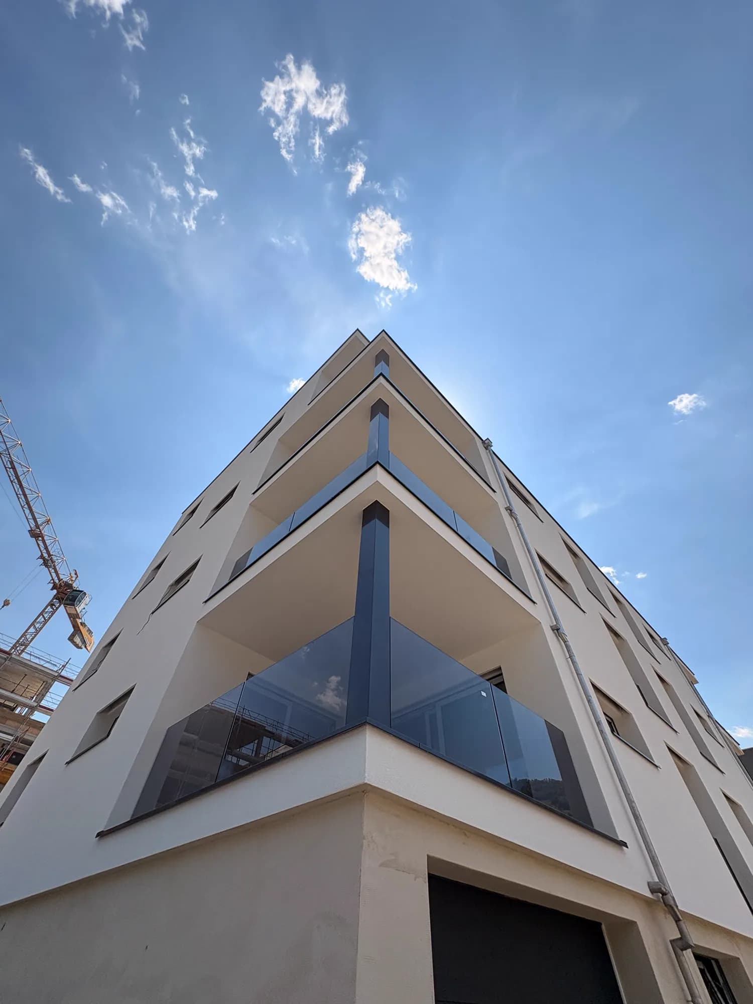 Angle d'un immeuble neuf avec garde-corps en verre fumé sur trois niveaux, flèche de grue à gauche