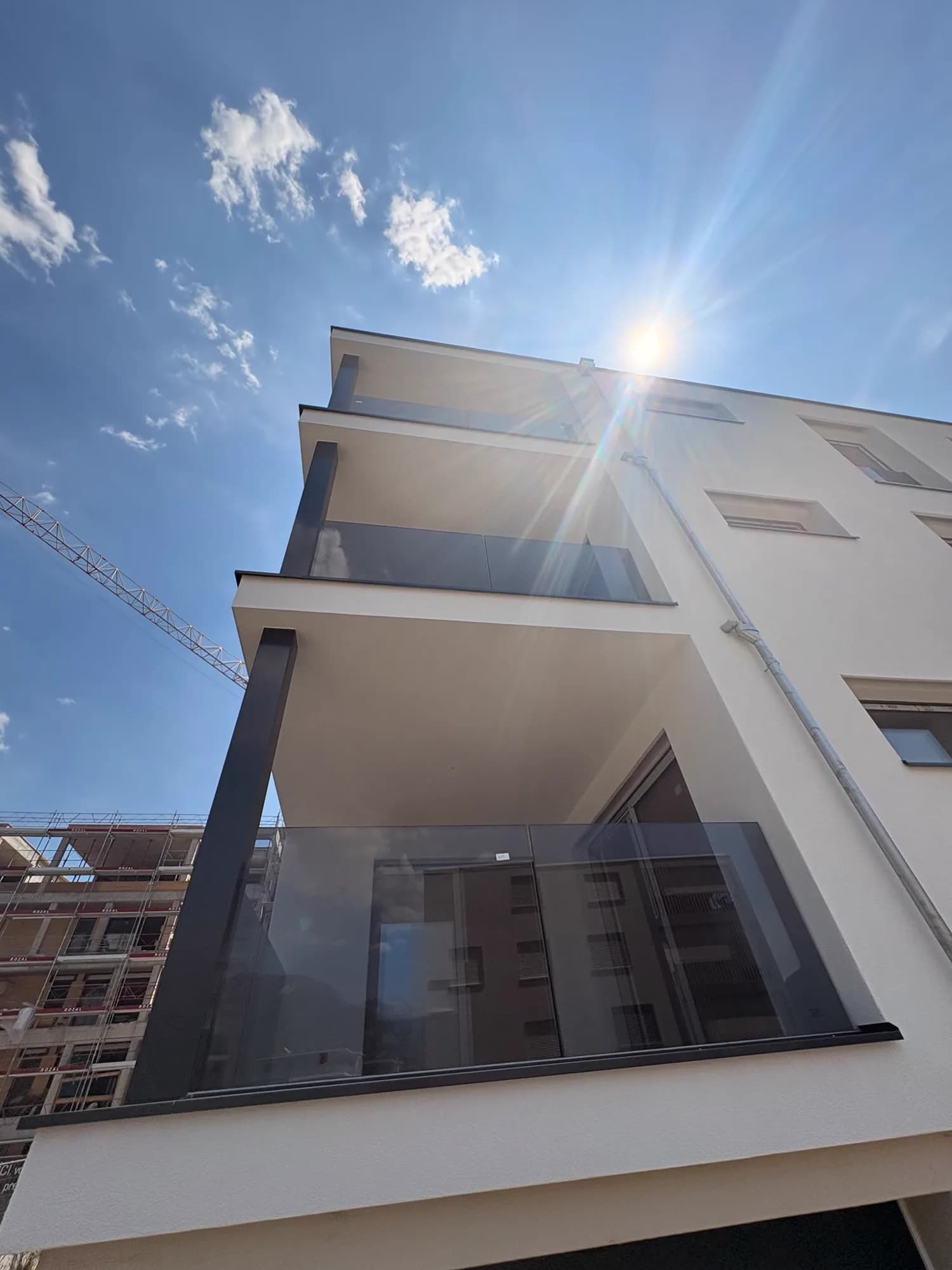 Façade d'immeuble vue en contre-plongée, garde-corps de balcon en verre fumé sur trois niveaux, grue de chantier à gauche