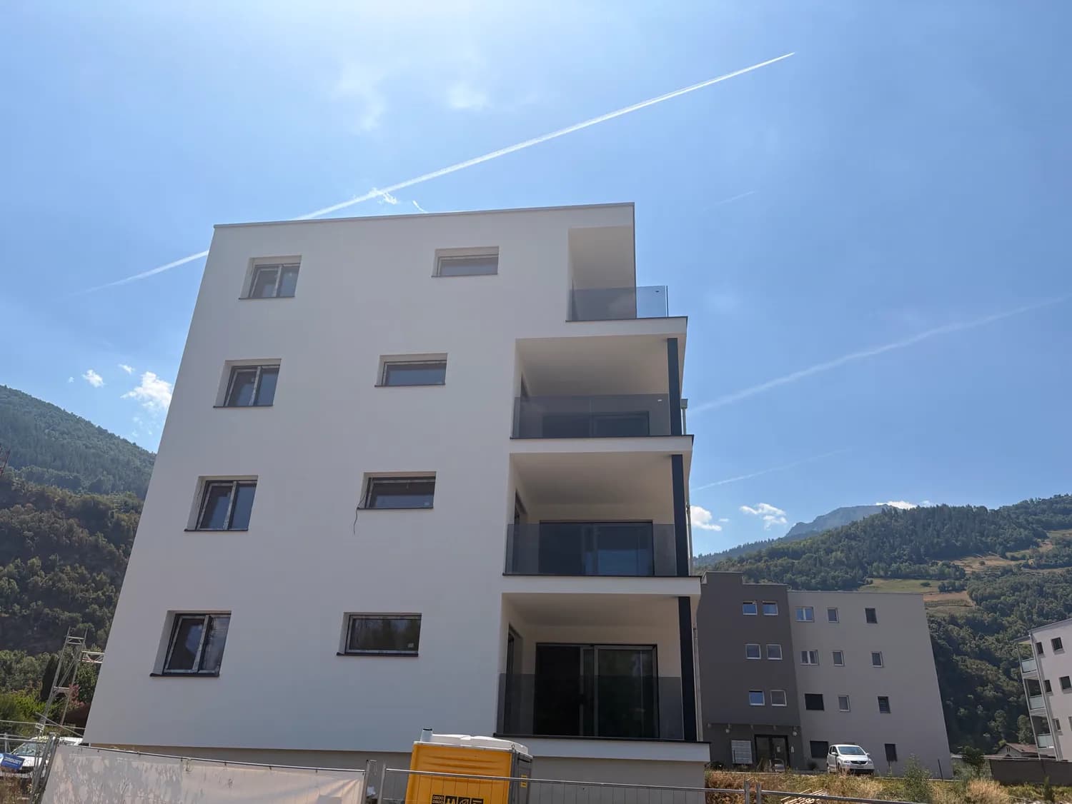 Immeuble neuf aux balcons équipés de garde-corps en verre fumé, coteau boisé en arrière-plan